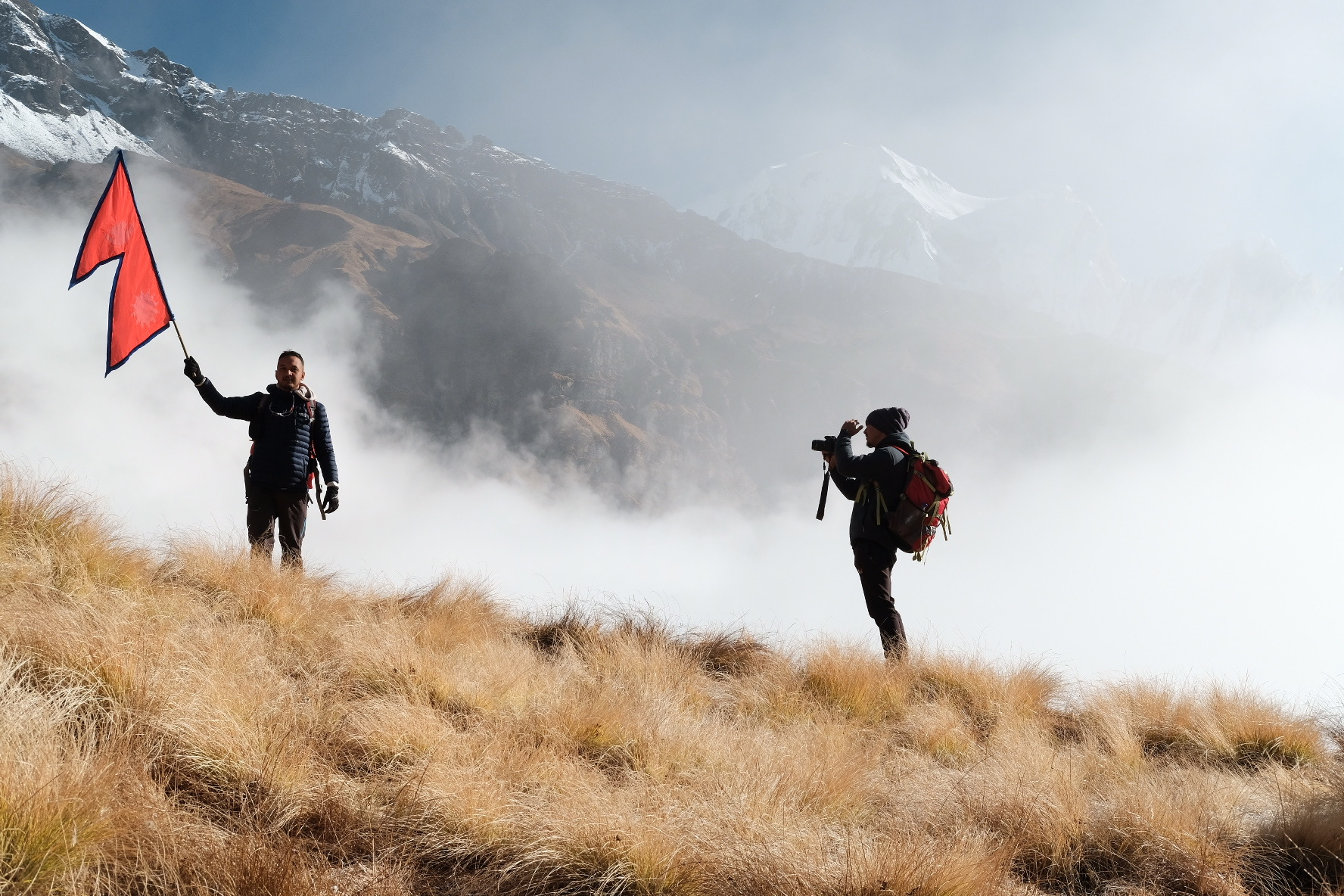 Himalayan trekking adventure — two hikers on misty mountain slope with Nepali flag