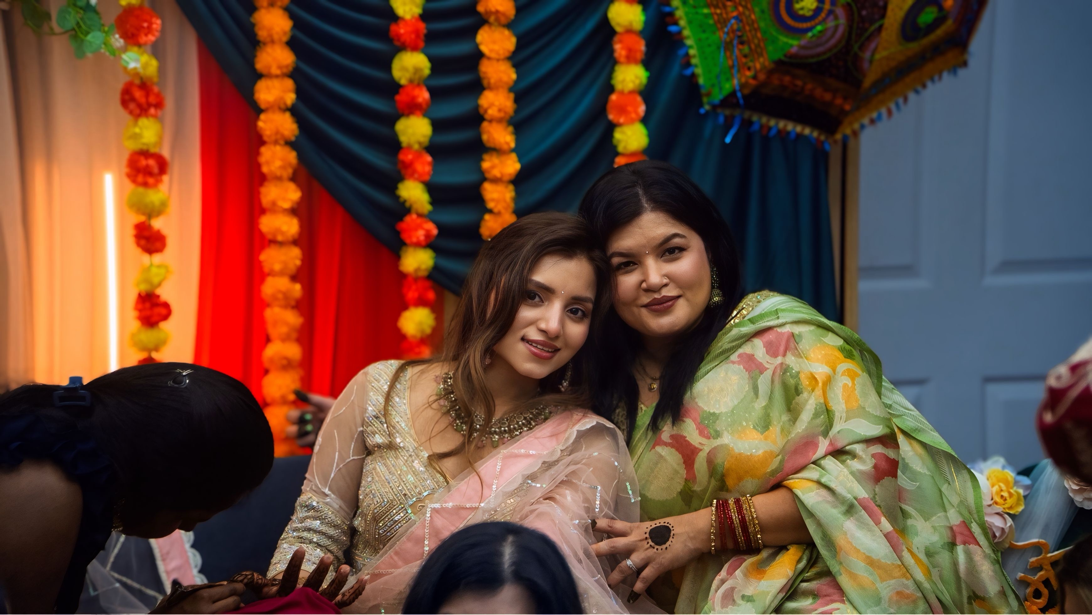 Mehndi celebration — two women at South Asian wedding with floral decorations